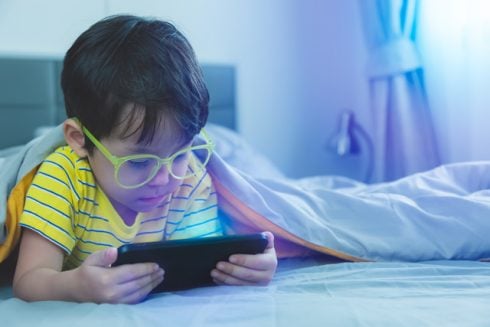 Cute Little Child Watch Movie On Smartphone At Bed  Dangers Of Blue Light Can Damage Eyes  Handsome Little Boy Can Be Age Related Macular Degeneration From Blue Light  Wear Eyeglasses Since Childhood